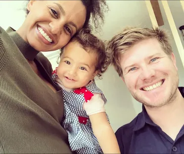 A happy couple poses with their smiley toddler, capturing a joyful family moment indoors.