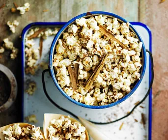Popcorn in a blue metal bucket with cinnamon sticks on a tray, seen from above.