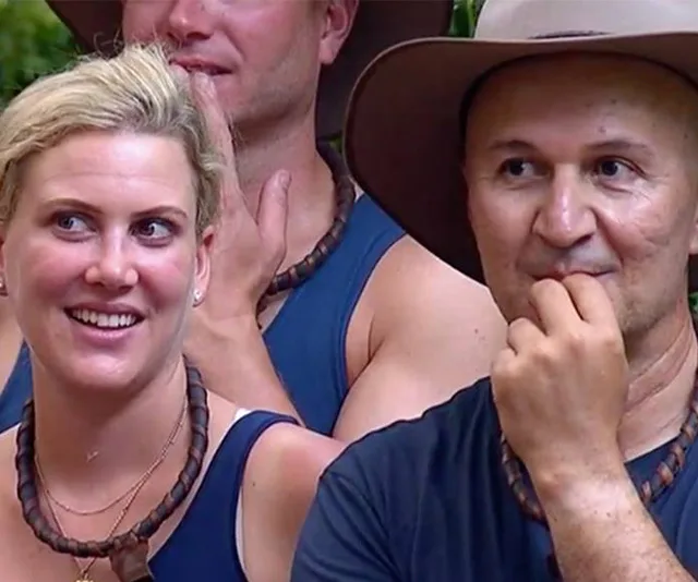 Contestants wearing blue tops and necklaces react during a challenge on "I'm a Celebrity" in the jungle setting.