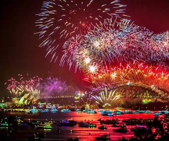 Fireworks light up the night sky above Sydney Harbour Bridge, with boats on the water during celebrations.