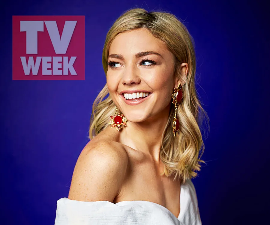 Blonde woman smiling in front of a blue background, wearing red earrings, with TV WEEK logo in the corner.