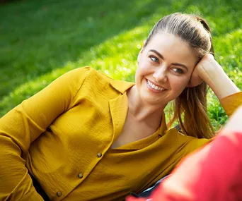 Smiling woman in a yellow shirt lying on grass.