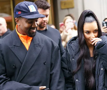 Couple smiling outside in casual winter outfits, with woman covering her mouth slightly.