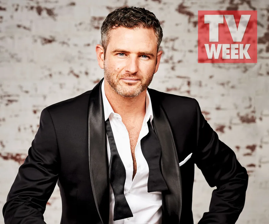 Man in a tuxedo poses confidently against a brick wall, with TV Week logo in the corner.