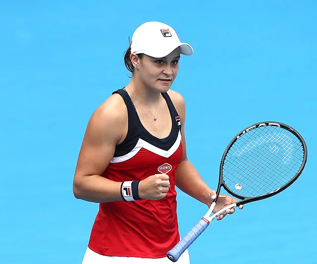 Ash Barty clenches fist, holding tennis racket, in red and black attire during Australian Open 2019 match.