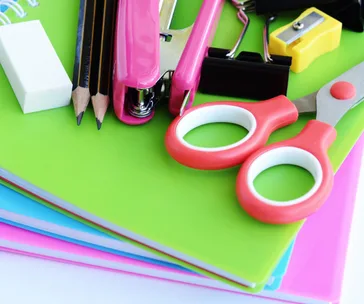 Colorful school supplies on notebooks: scissors, stapler, pencils, eraser, and sharpener.