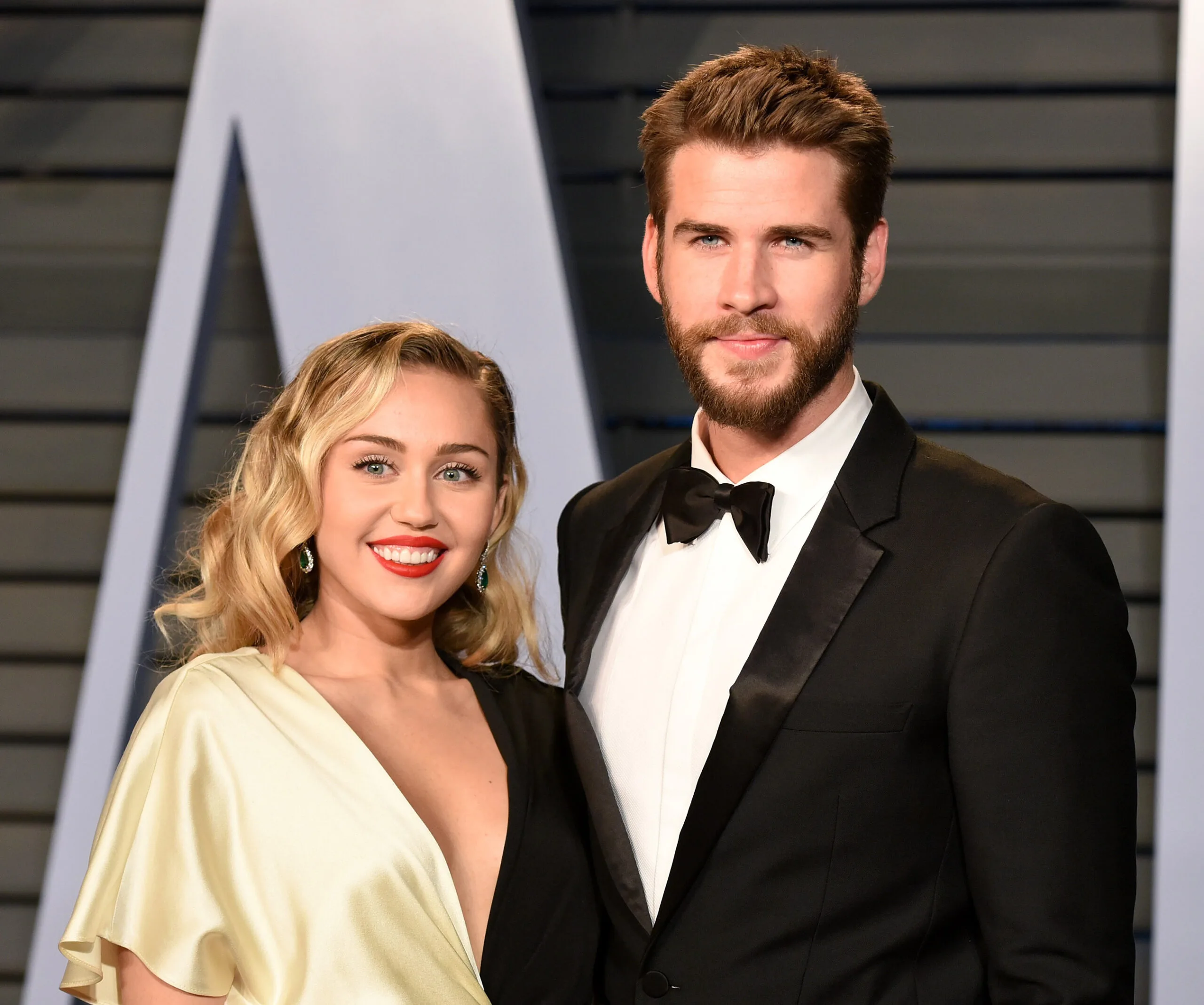 A couple posing elegantly on the red carpet, both dressed in formal attire with smiles.
