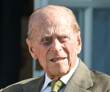 Elderly man in a suit and tie with a serious expression, outdoors.