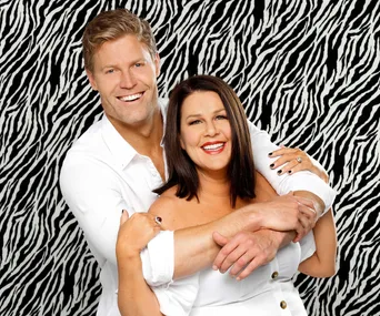 Two smiling people in white outfits hugging against a zebra print background.