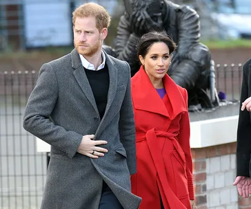 A man and woman in formal winter coats walk together outdoors near a statue.