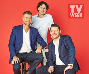 "Three men in blazers sit and stand against a red background with a TV Week logo."