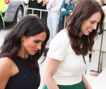 Two women walking together, smiling, surrounded by people in the background.