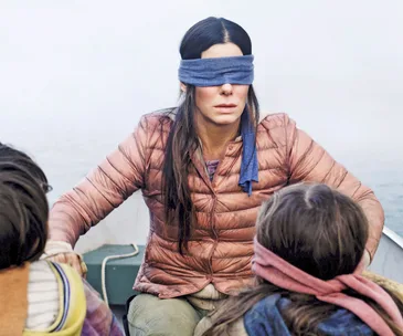 A blindfolded woman in a boat with two children, from the movie Bird Box.