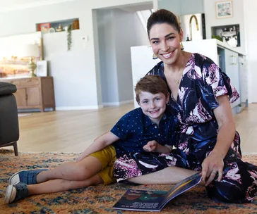 Mother and son sitting on the floor, smiling, while looking at a book together in a cozy living room.