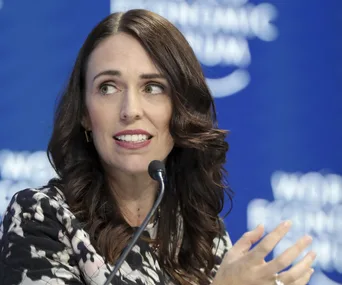 A person with long dark hair speaking at a conference, with a blurred blue background displaying "World Economic Forum."