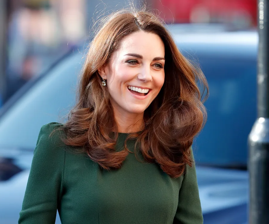 A woman with long brown hair wearing a green dress, smiling outdoors.