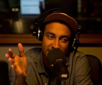 Man wearing headphones, speaking into a microphone in a recording studio.