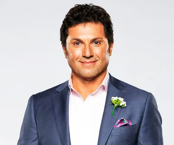 Man in a suit with boutonniere smiling against a neutral background.