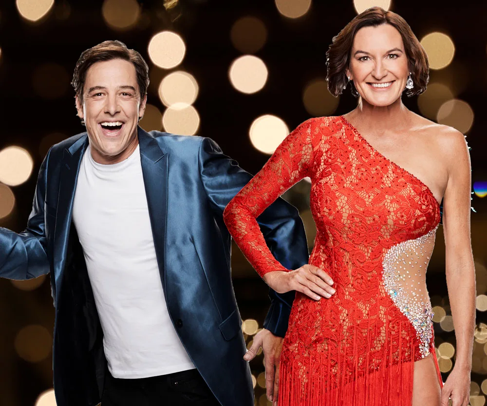 Two people smiling against a bokeh background. One wears a blue jacket, and the other is in a red, one-shoulder dress.
