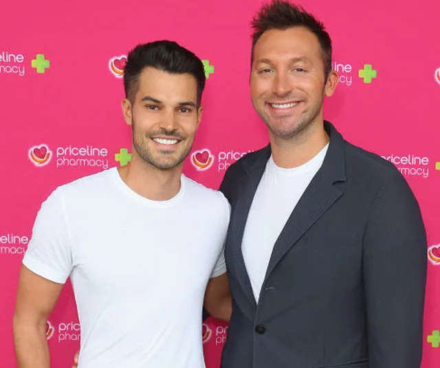 Two individuals smiling at a Priceline Pharmacy event with a pink branded backdrop.
