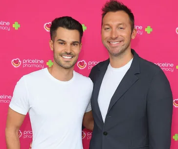 Two individuals smiling at a Priceline Pharmacy event with a pink branded backdrop.