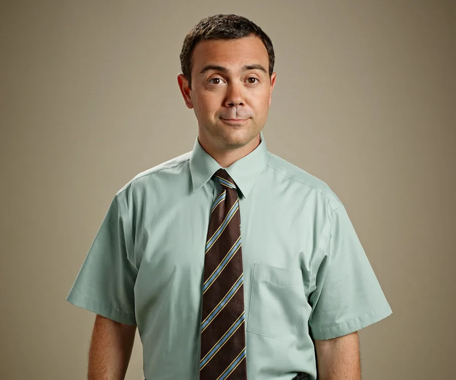 Man in a light green shirt and striped tie against a plain background, with a neutral expression.