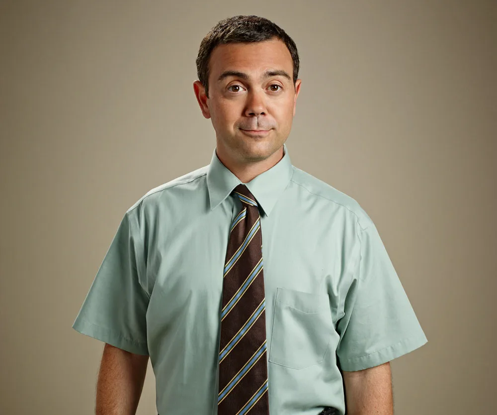 Man in a light green shirt and striped tie against a plain background, with a neutral expression.