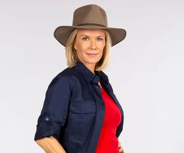 Blonde woman in a navy shirt and wide-brimmed hat, posing confidently against a neutral background.