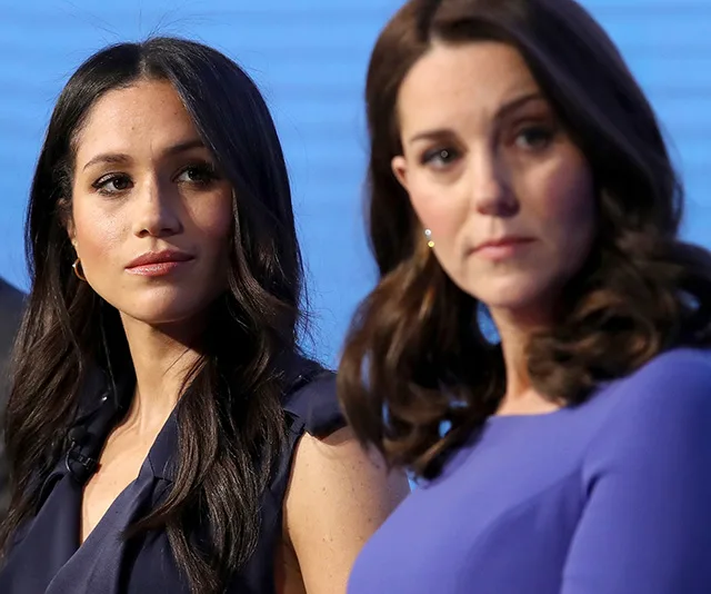 Two women in blue outfits looking in opposite directions at an event.