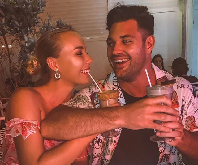 A couple smiles and shares drinks at an outdoor setting, appearing happy and relaxed.