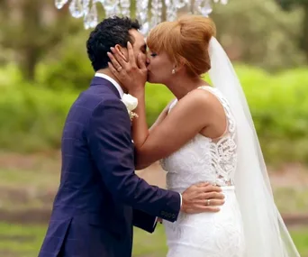Bride and groom in wedding attire share a kiss outdoors.