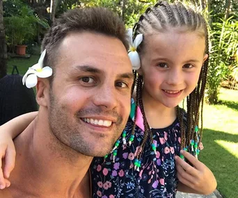 A man and a young girl smiling outdoors, both with flowers in their hair.