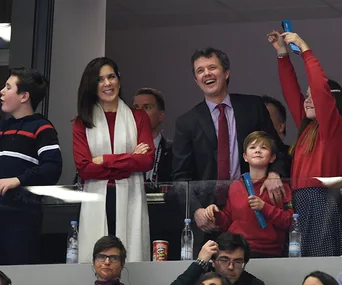 Crown Princess Mary and family enjoy a handball game, smiling and cheering from a stadium box.