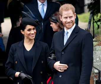 A smiling couple in elegant winter attire at an outdoor event, surrounded by other people.