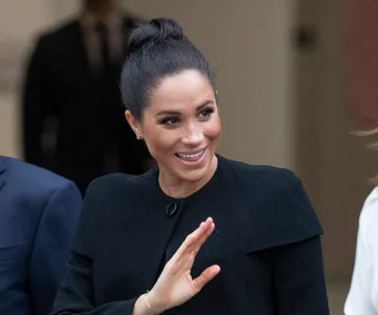Meghan Markle smiling and waving in a black Givenchy coat.