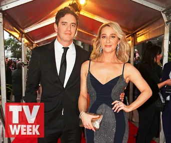 Two well-dressed individuals posing on a red carpet at an event, one in a suit and the other in a formal gown.