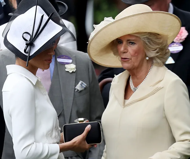 Women in formal attire and hats engaged in conversation at an outdoor event.