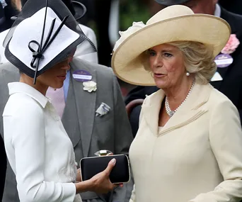 Women in formal attire and hats engaged in conversation at an outdoor event.