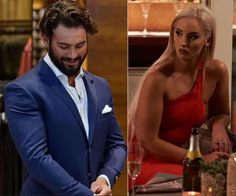 Two people from a reality show scene. One man in a blue suit, smiling, and one woman in red, sitting and looking focused.