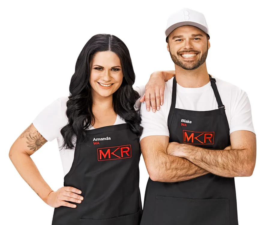 Two people wearing "MKR" aprons, one with tattoos, smiling, arms linked.