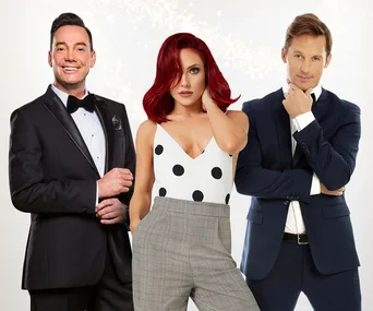 Three people posing; a man in a black tuxedo, a woman with red hair in a polka dot top, and a man in a navy suit.