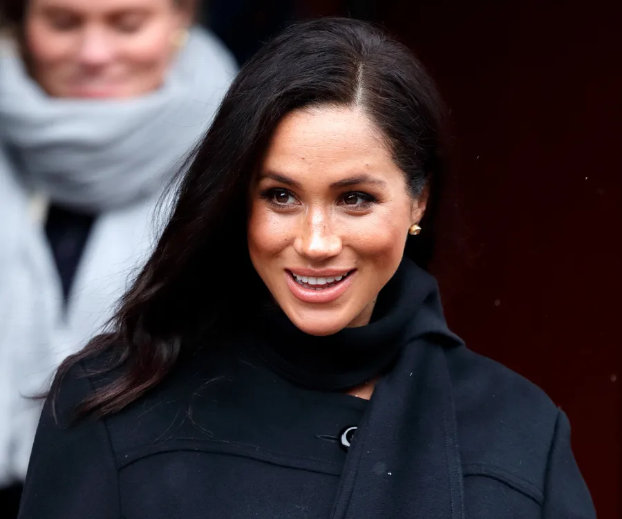Alt text: "Woman with long hair and a black coat smiling outdoors."