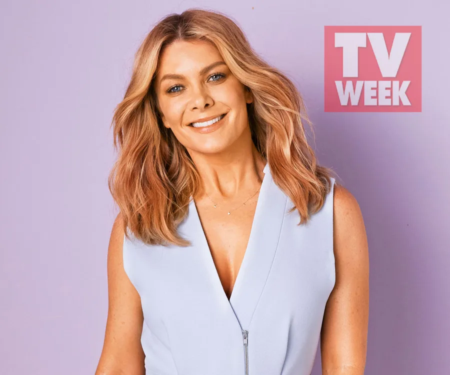 A person with wavy blond hair in a sleeveless light blue top smiles against a purple background with a TV Week logo.