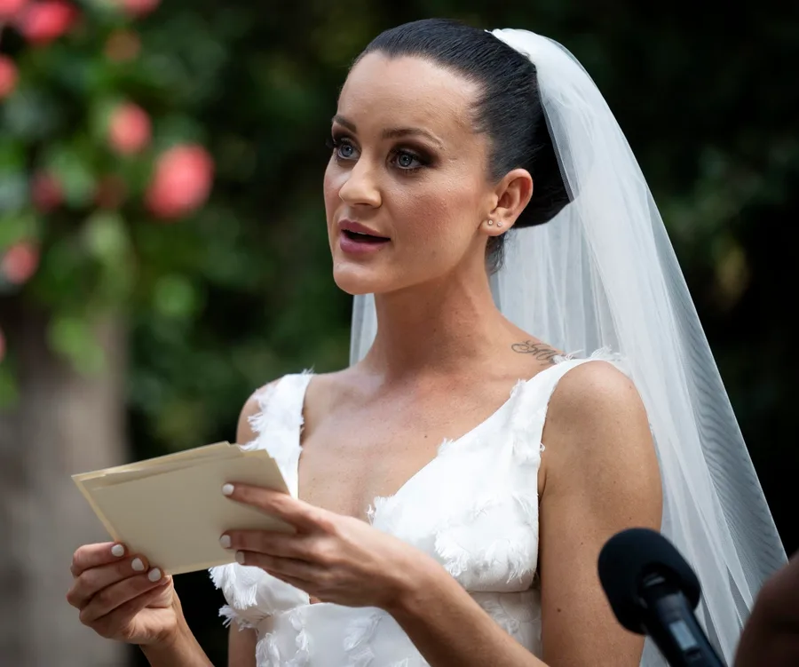 Bride in wedding dress and veil reading vows outdoors.
