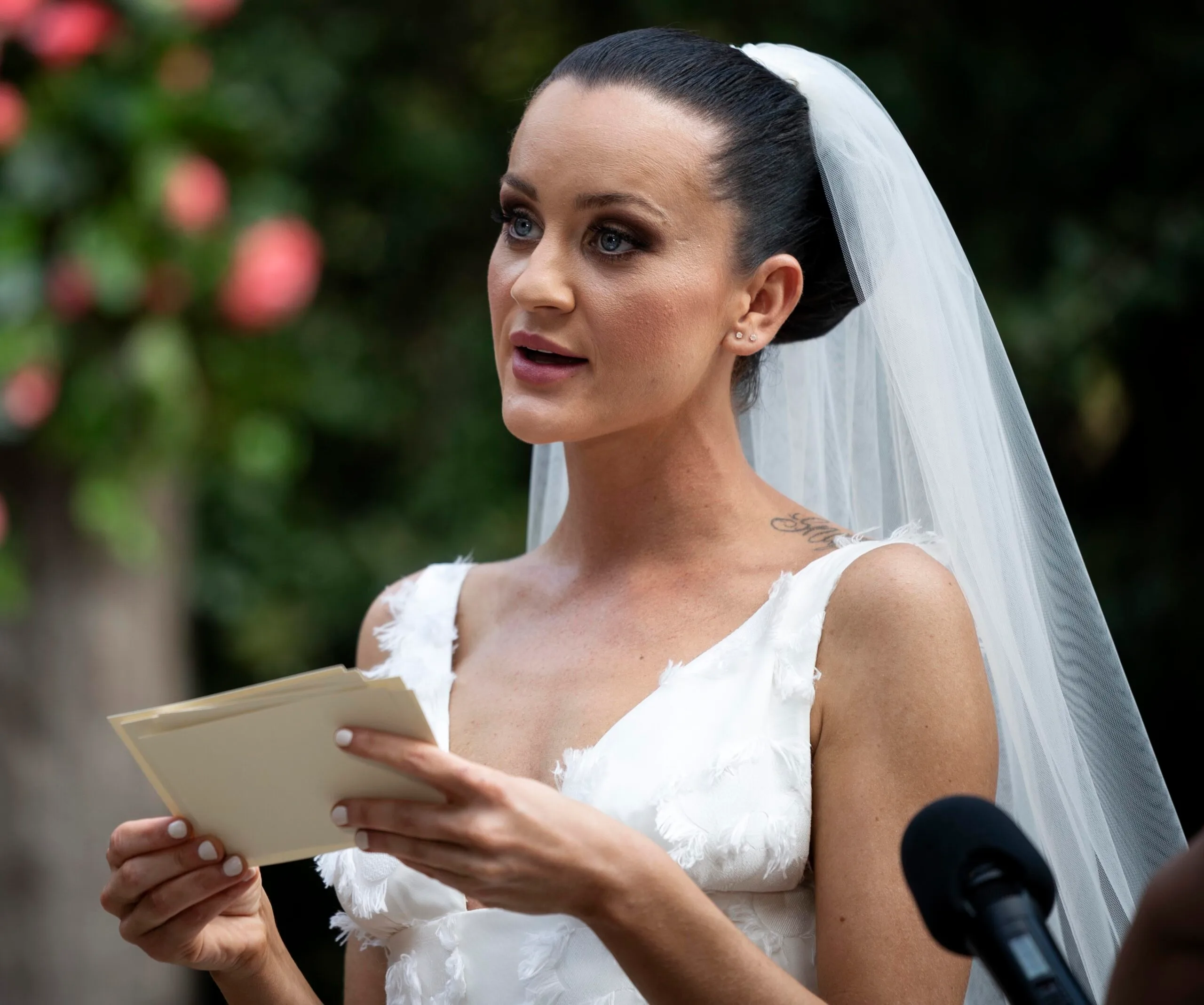Bride in wedding dress and veil reading vows outdoors.