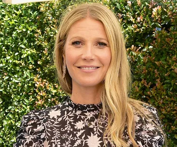 I don't know who this is, but it's a person with long blonde hair in a floral outfit, smiling against a green leafy background.
