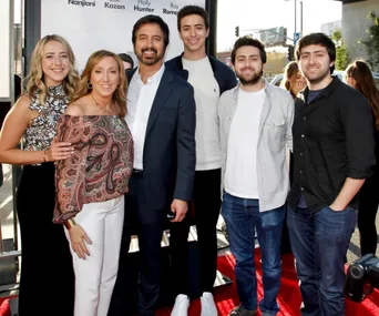 Family photo of six people smiling on a red carpet at an event.