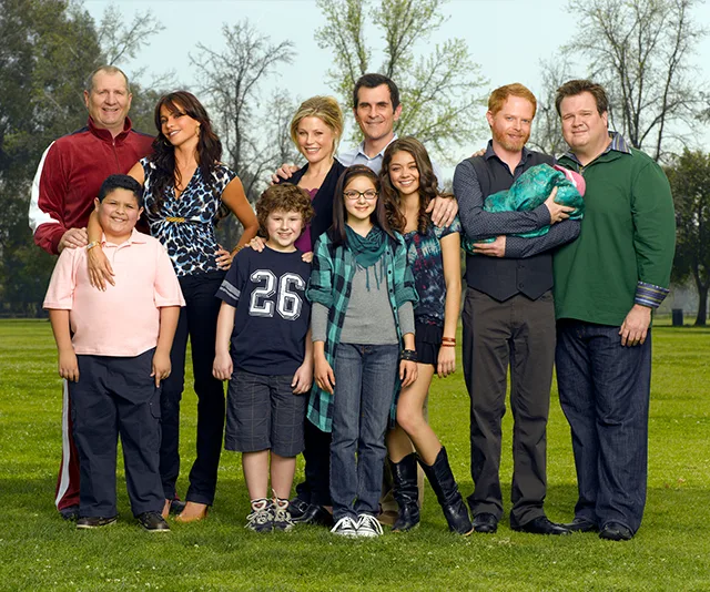 "Modern Family cast posing together in a park, smiling and standing in a group."