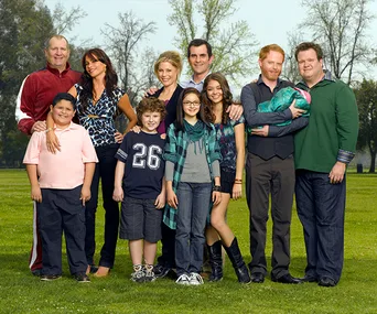 "Modern Family cast posing together in a park, smiling and standing in a group."
