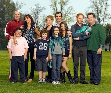 "Modern Family cast posing together in a park, smiling and standing in a group."
